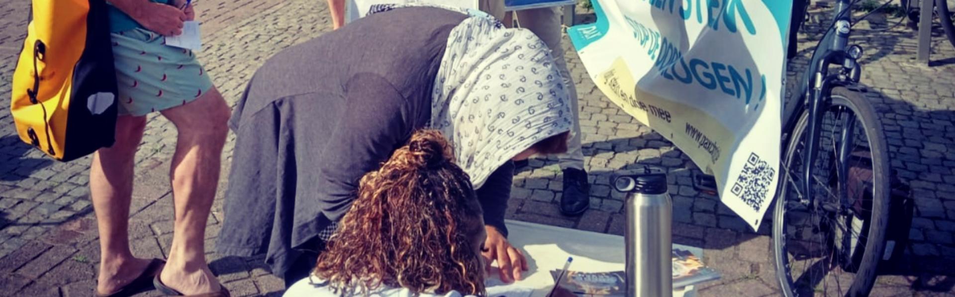 Mensen tekenen een petitie tegen de oorlogseconomie aan de bib van Sint-Niklaas.