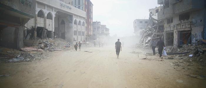 man wandelt op grote lege straat tussen kapotgeschouten gebouwen