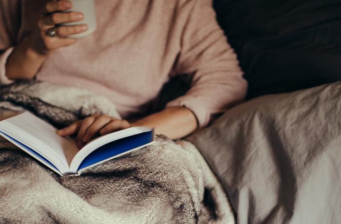 Vrouw met koffie in rechterhand leest een boek in bed