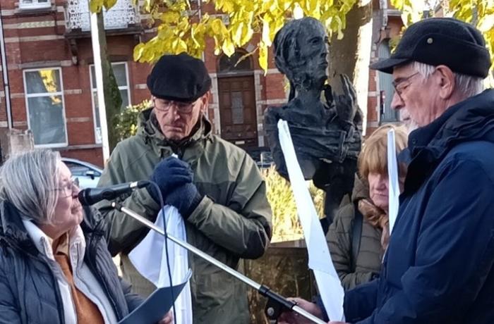 twee mannen en twee vrouwen met witte vlaggen staan bij het beeld voor de onbekende oorlogsvrouw in Hasselt. Warm ingeduffeld (de mannen dragen petten).
