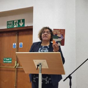 Bénédicte Kusendila rapporteert aan de Europese Conferentie, houdt een Nederlandstalige kopie van het Manifest voor Vrede omhoog